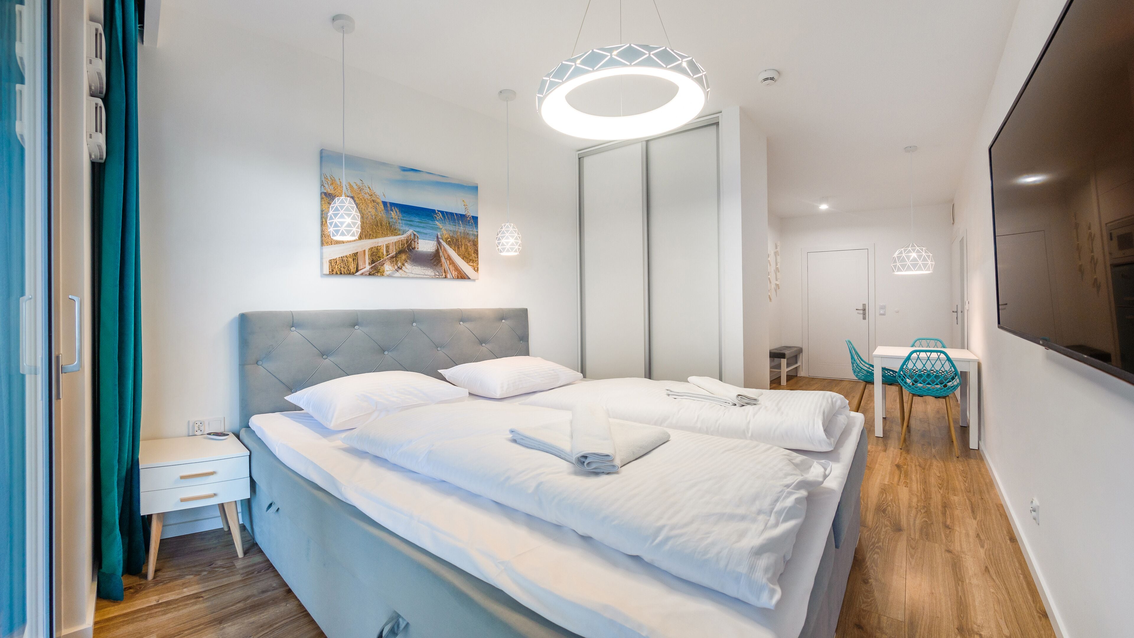 A modern hotel room with a large bed, a desk, and a chair. There is a painting on the wall and a large mirror.