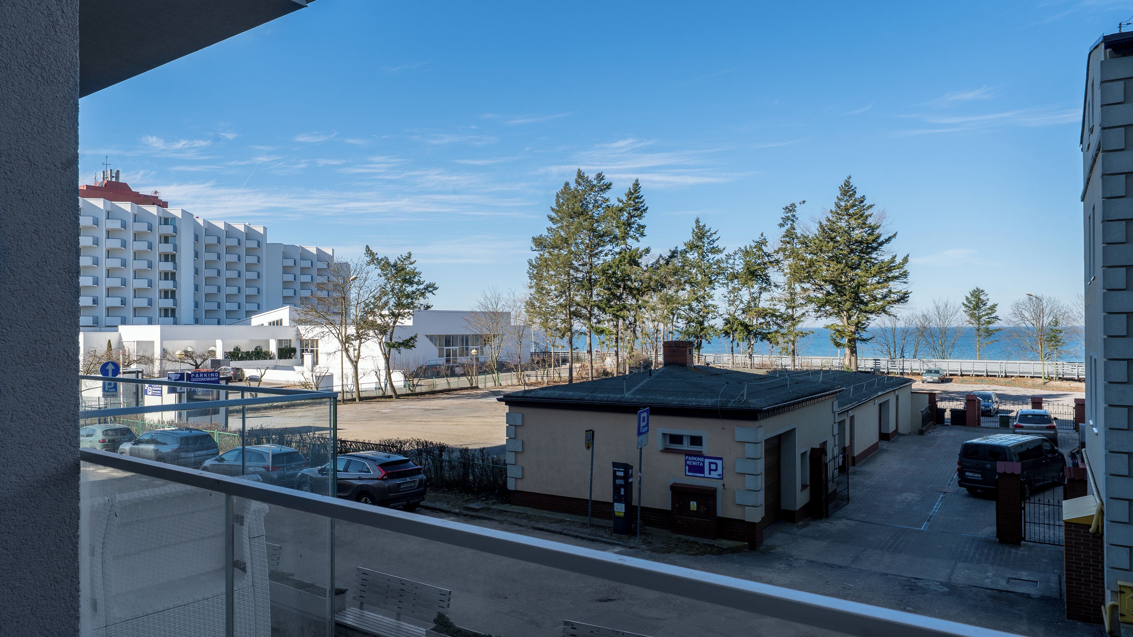 A parking area with cars, a building with a sign, and trees in the background.
