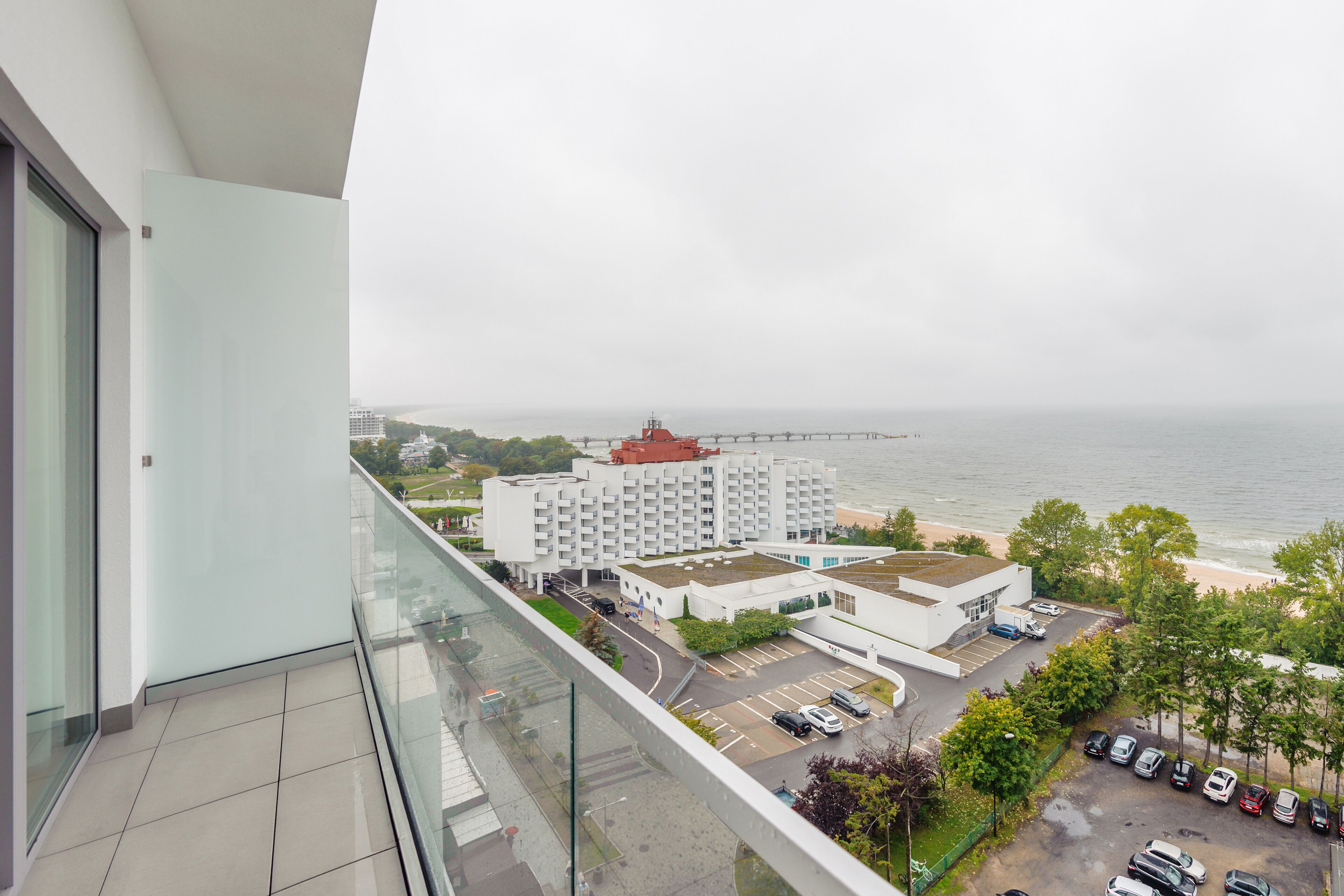 Un edificio alto con vistas al mar, una zona de estacionamiento y un hotel con techo rojo.