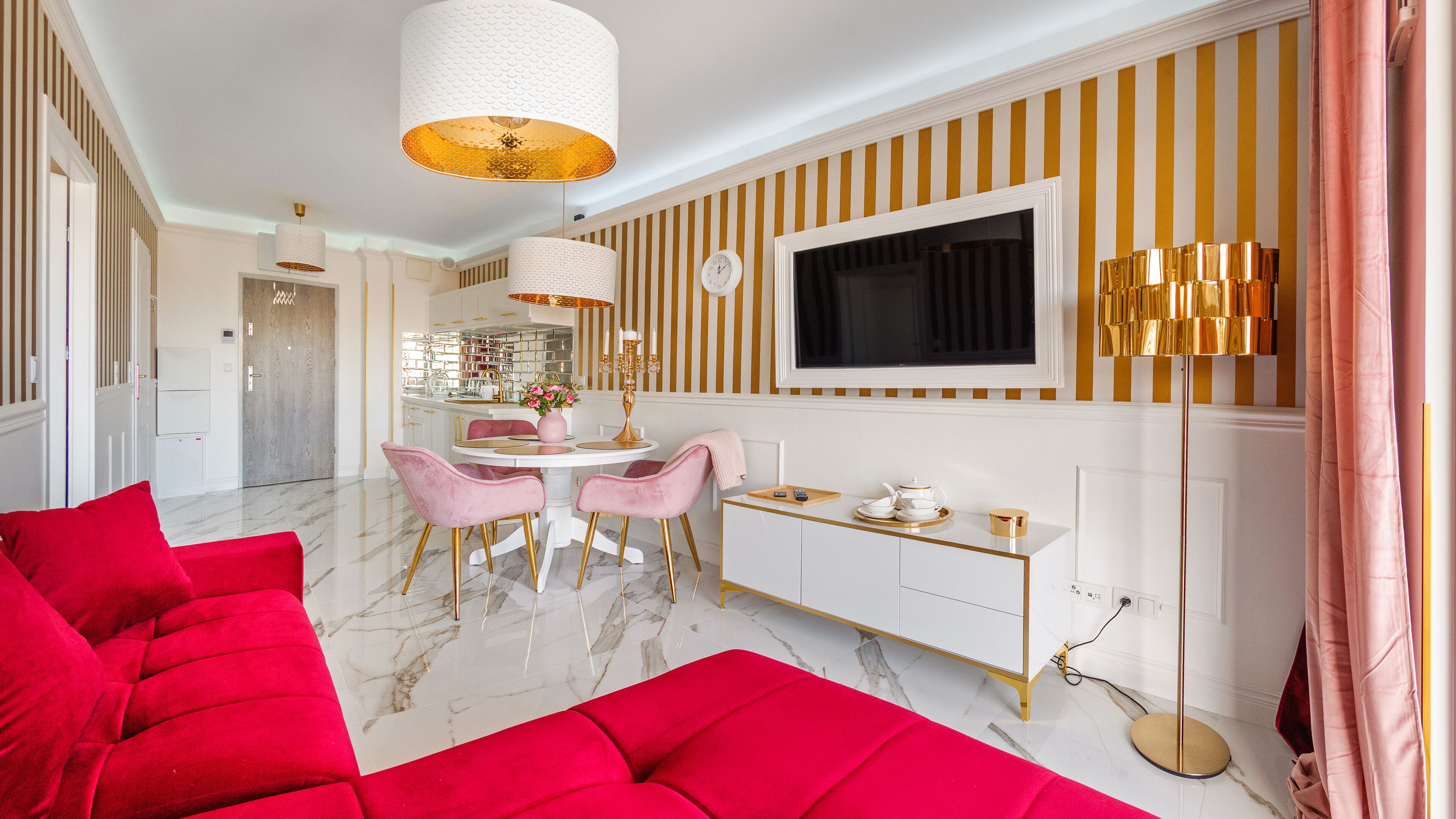 A modern living room with a red sofa set, a dining area with pink chairs, and a kitchen in the background.