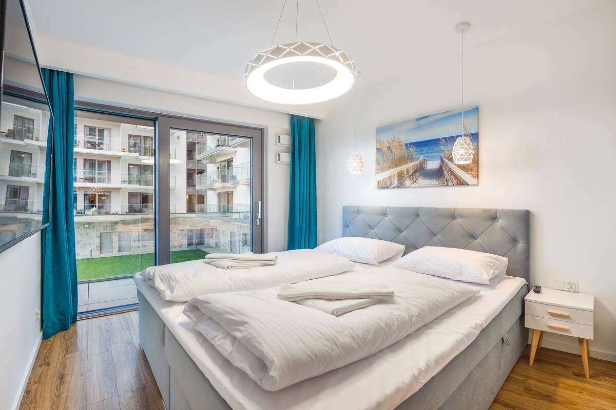 Une chambre d’hôtel moderne avec un grand lit, une vue sur la façade de l’immeuble et un tableau accroché au mur.
