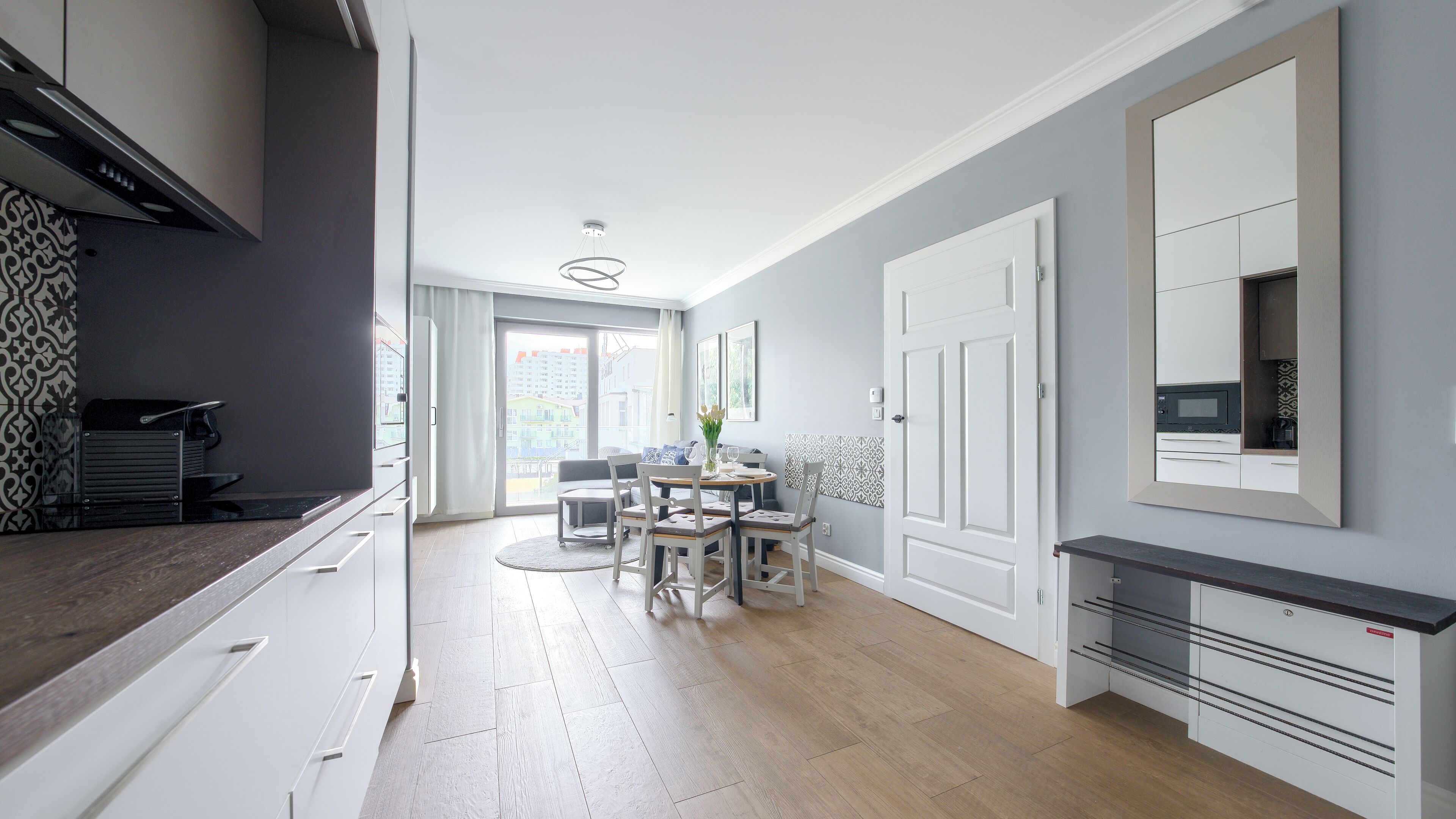 A modern kitchen with white cabinetry, a dining area with a round table and chairs, and a large window providing natural light.