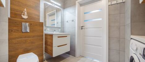 Un bagno moderno con un mobile bagno in legno, un water, uno specchio e una lavatrice.