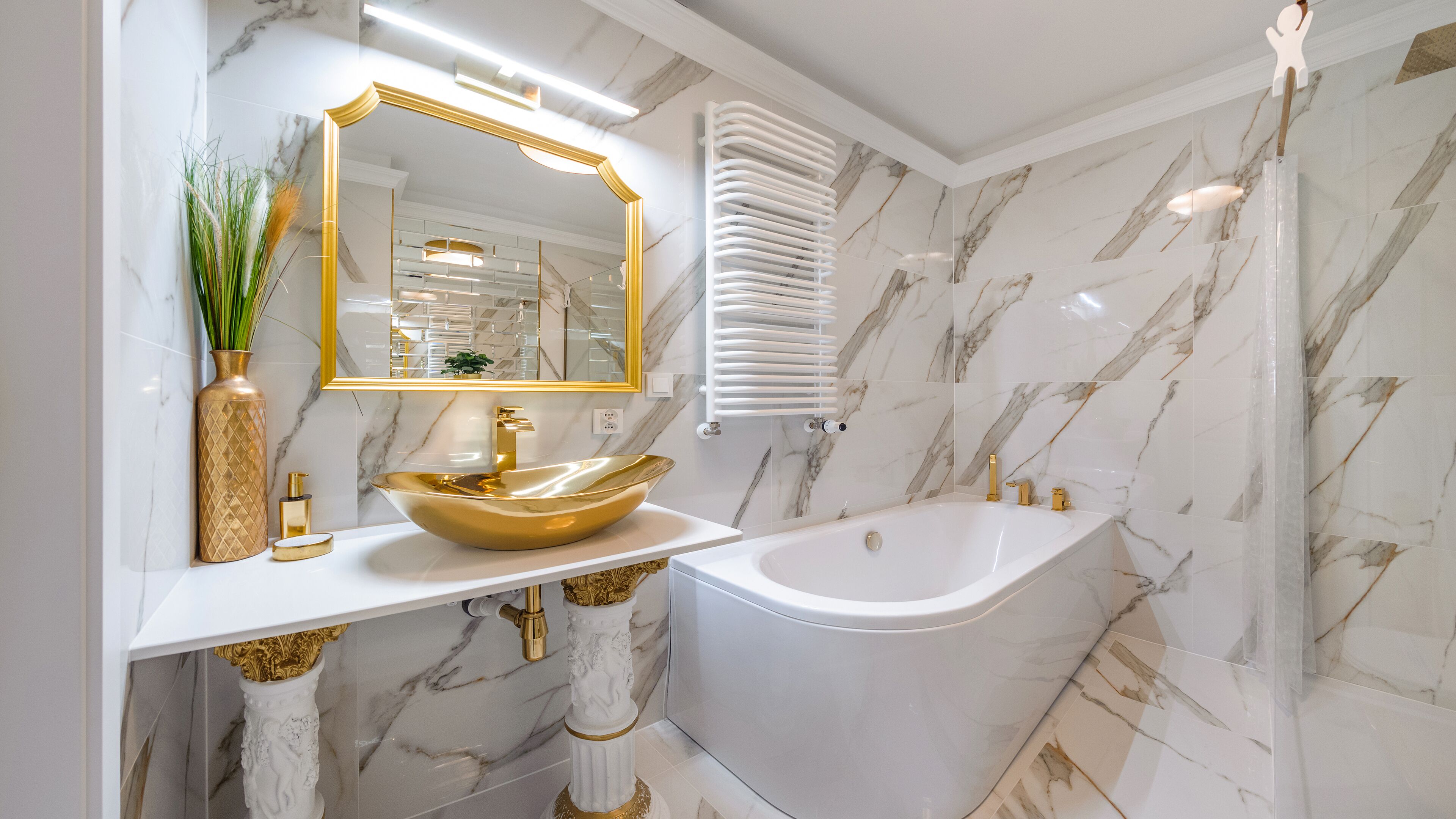 Une salle de bain avec un lavabo doré, un grand miroir et une baignoire.