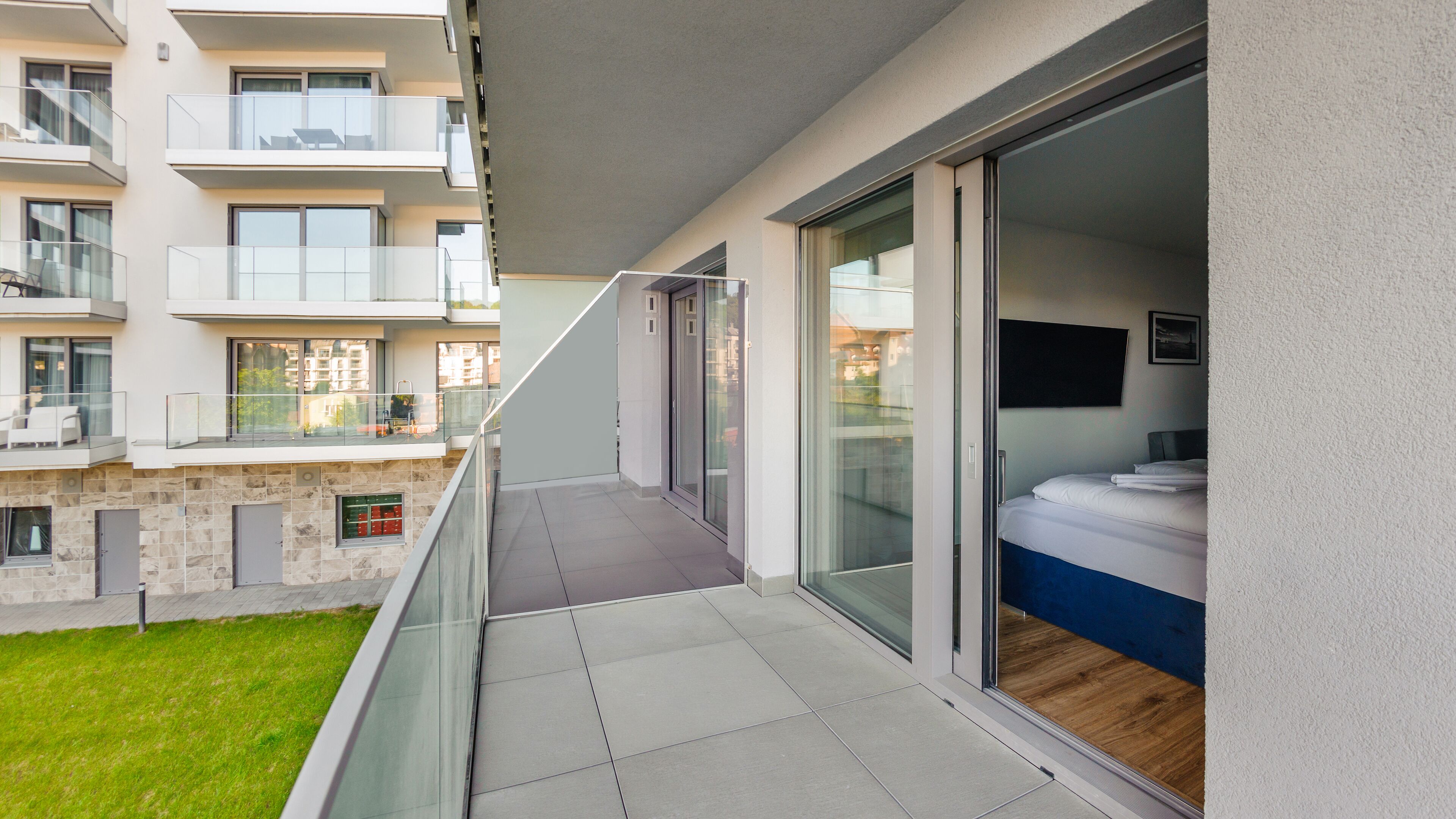 A modern apartment with a balcony, large windows, and a view of neighboring buildings.