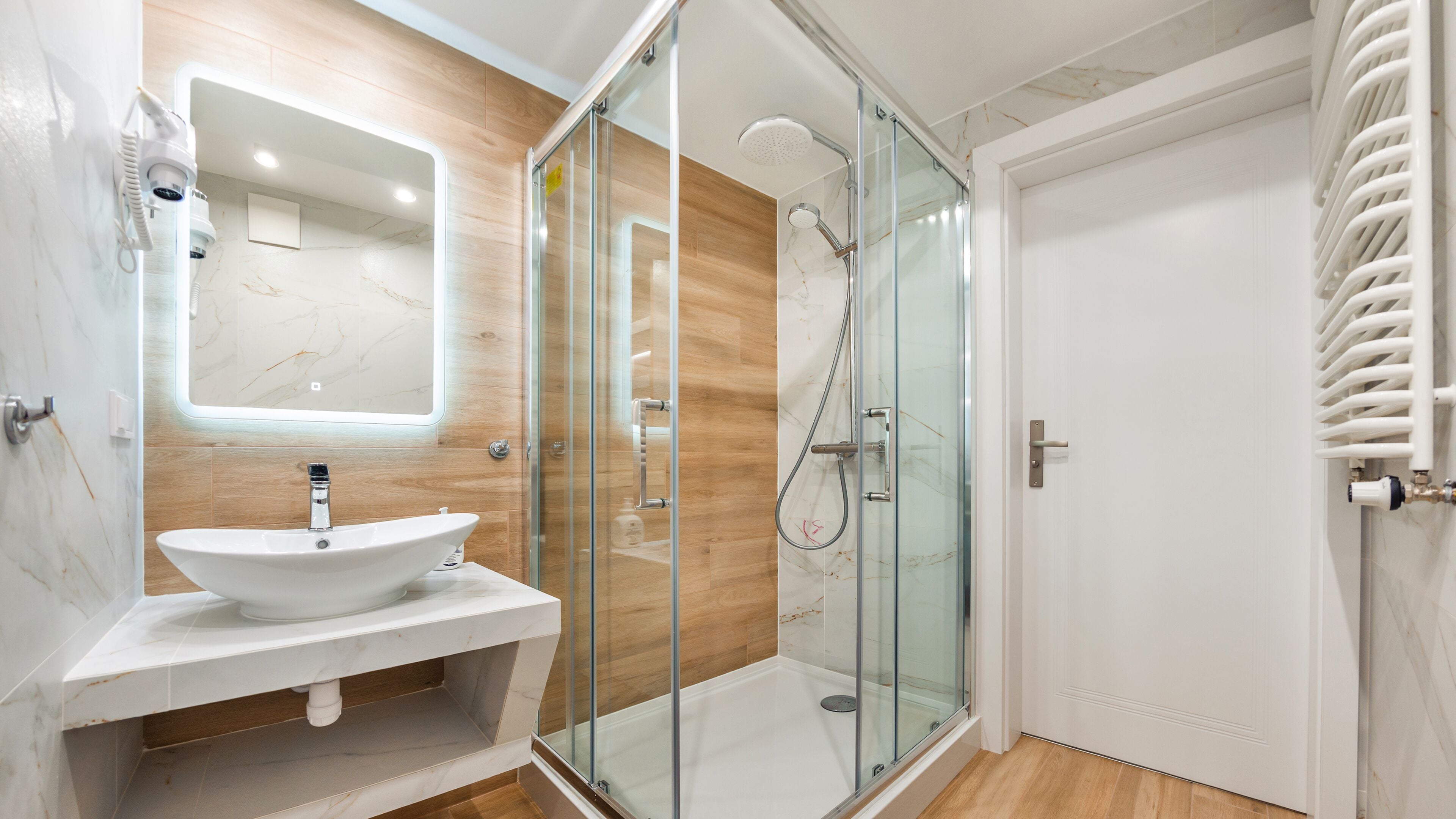 Ein modernes Badezimmer mit einer Duschkabine, einem weißen Waschbecken und einer Holzausstattung.