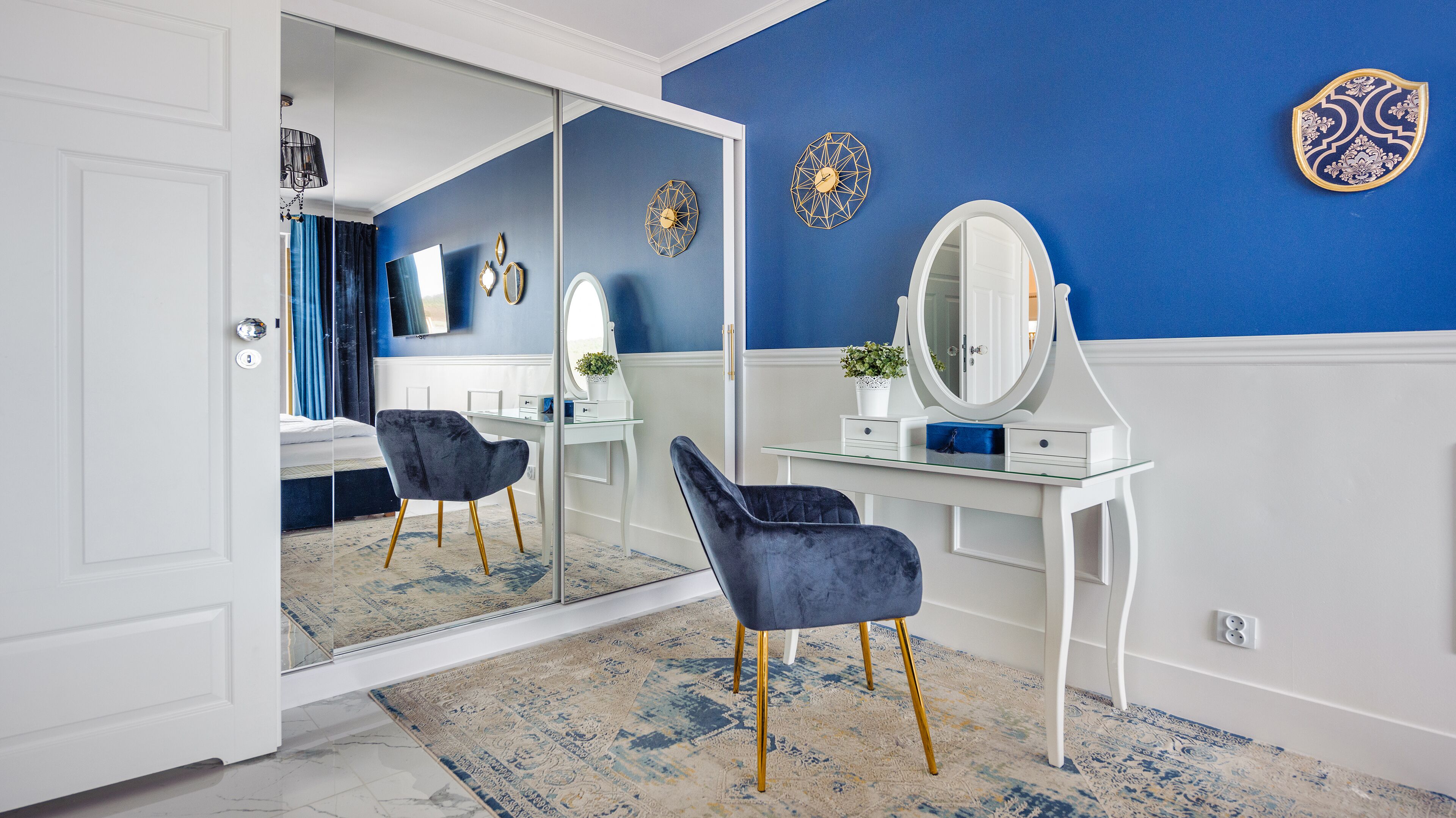 Una habitación con un tocador blanco, un espejo, una pared de acento azul y un espejo grande en la entrada.