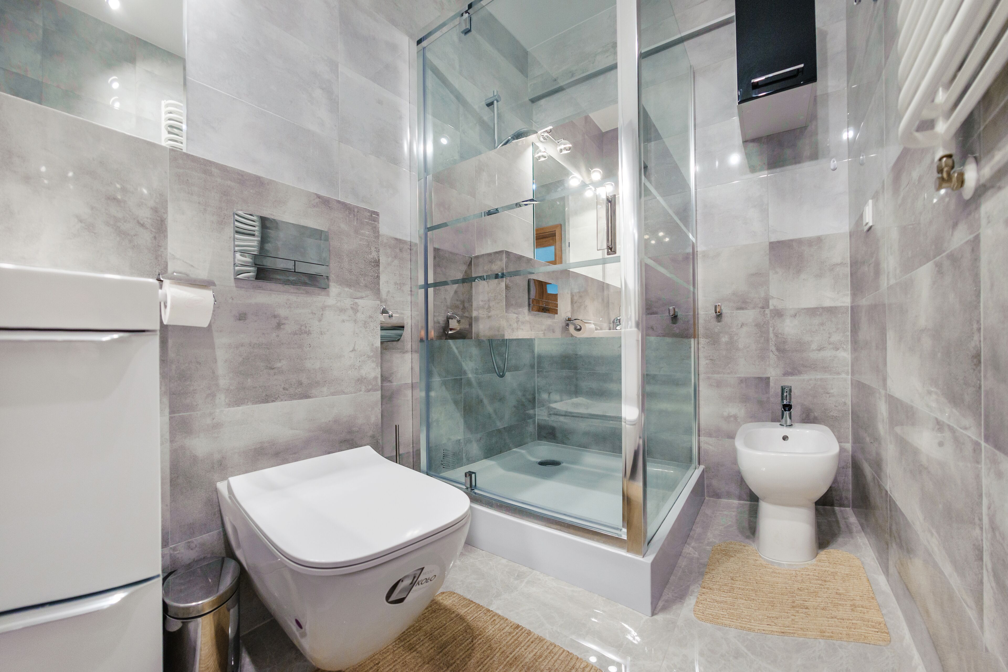A modern bathroom with a glass-enclosed shower, a toilet, and a bidet.