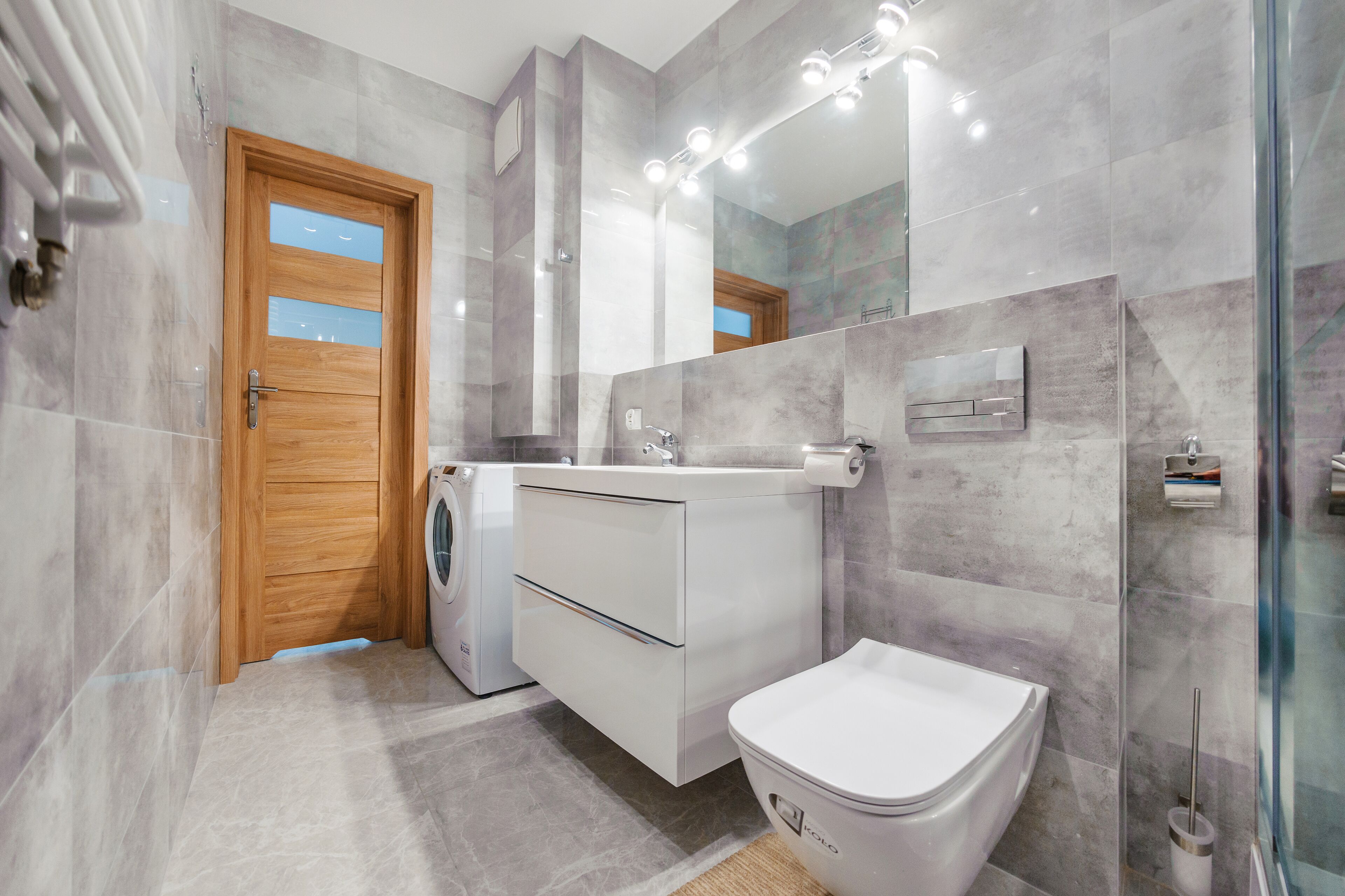 Ein modernes Badezimmer mit Holztür, Waschmaschine, Toilette und einer Duschkabine aus Glas.