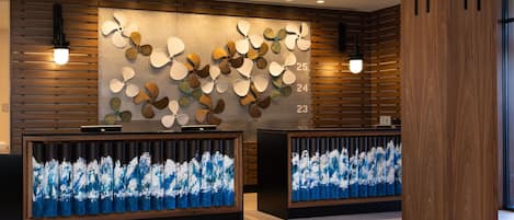 A reception area with wooden paneling, a wall-mounted fan display, and two reception desks with blue and white abstract art.