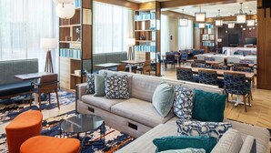A modern hotel lobby with a sofa, chairs, a coffee table, and a bookshelf. - Homewood Suites by Hilton Boston Seaport District (Boston)
