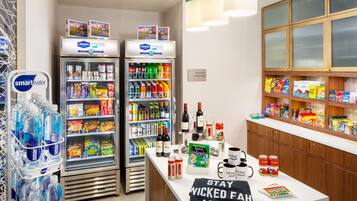 A hotel reception area with two refrigerators stocked with beverages, snacks, and a coffee machine. There is a sign indicating the availability of a suite shop.