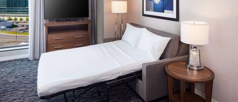A hotel room with a bed, a TV, a lamp, and a framed picture on the wall.