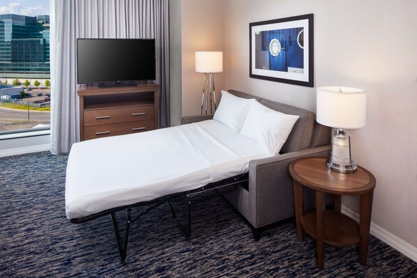 Habitación de hotel con cama, televisión, lámpara y un cuadro en la pared.