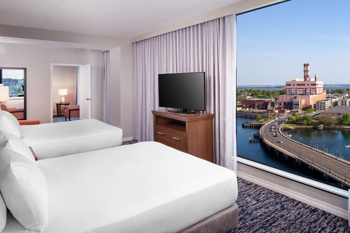 Ein Hotelzimmer mit zwei Betten, einem Fernseher und Blick auf Stadt und Wasser.