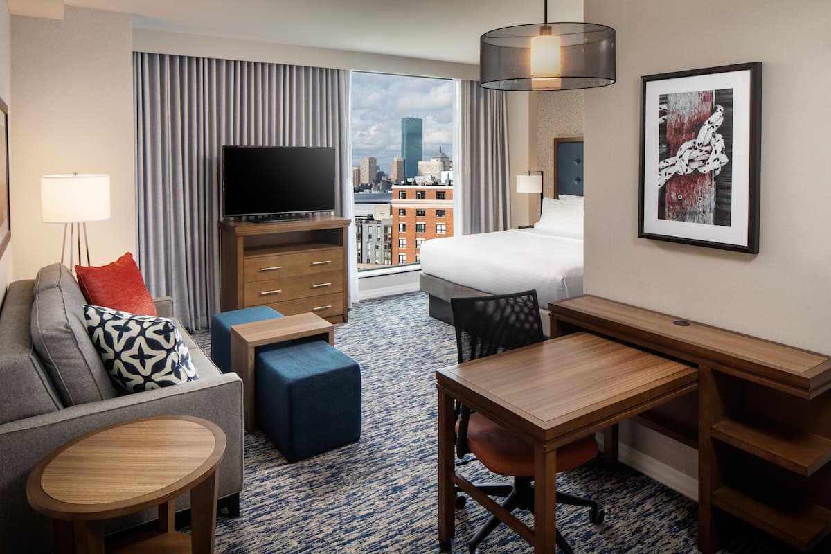 Ein Hotelzimmer mit Bett, Schreibtisch, Sofa, Fernseher und Blick auf die Stadt.