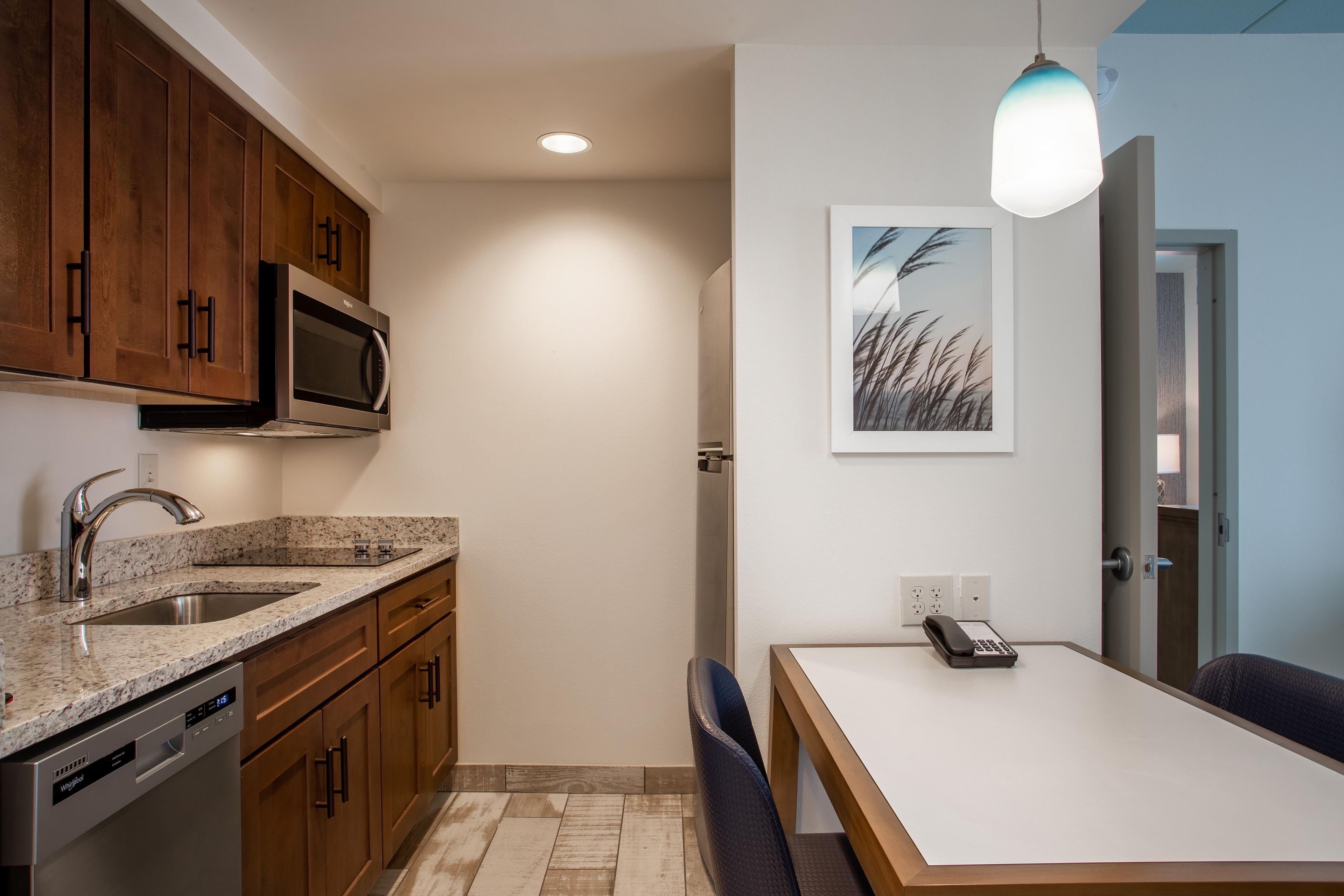 A modern kitchen with wooden cabinets, a built-in microwave, a granite countertop, and a dining area with a table and chairs.