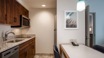 A modern kitchen with wooden cabinets, a built-in microwave, a granite countertop, and a dining area with a table and chairs.