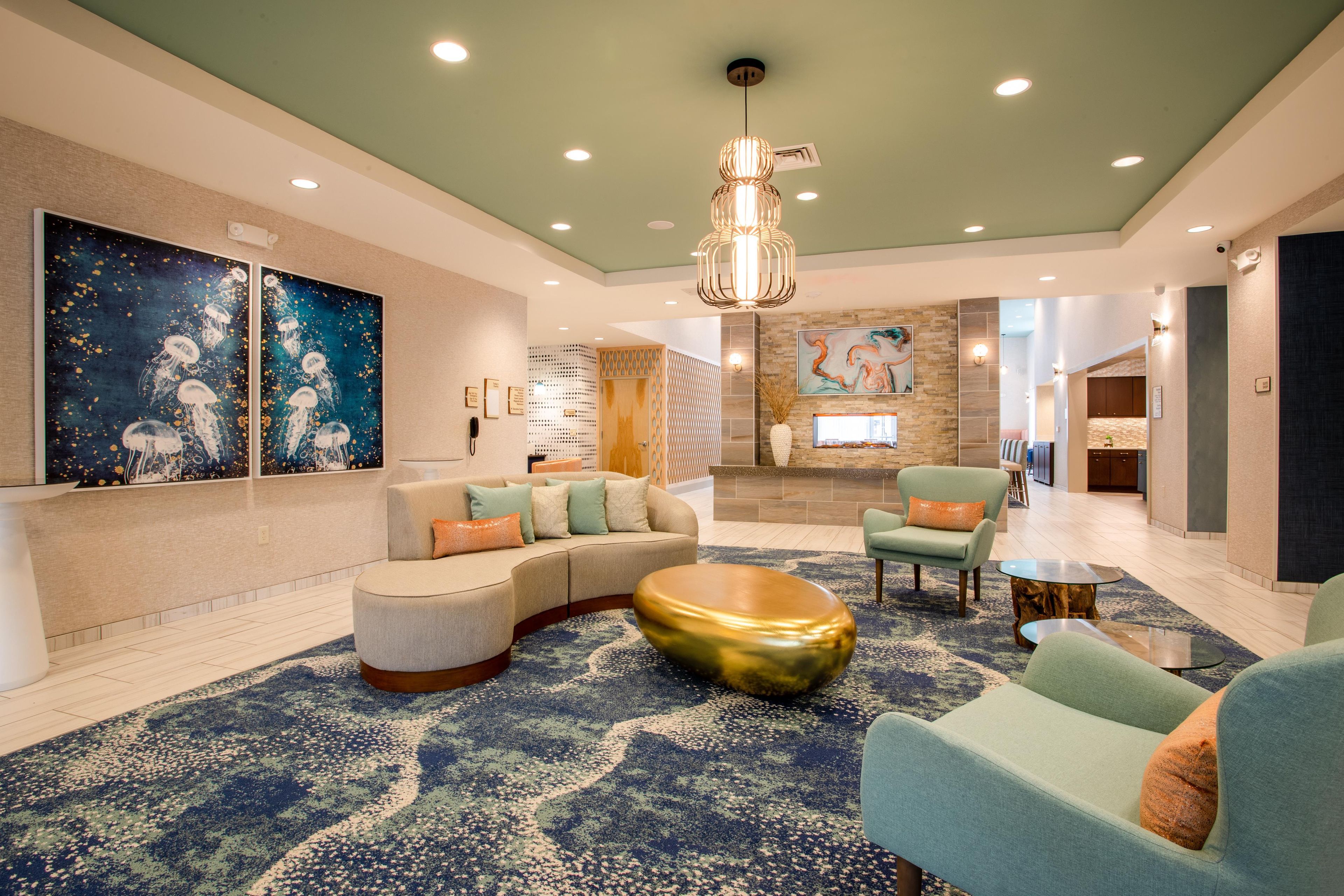 A spacious lobby with a curved sofa, a round gold coffee table, and a large abstract painting on the wall.