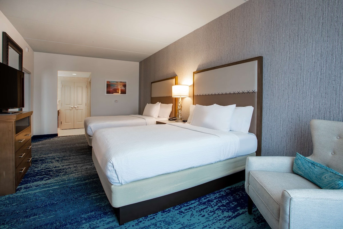 A hotel room with two beds, a TV, a desk, and a chair.