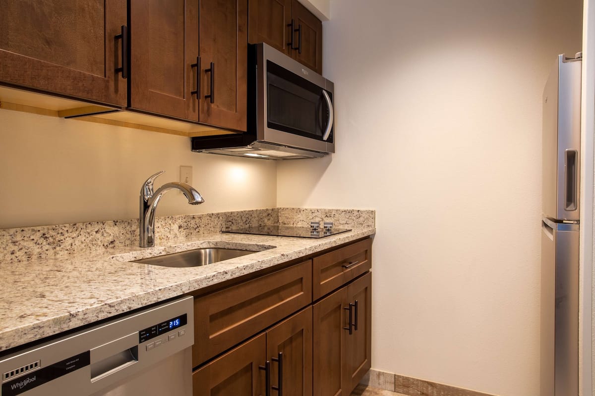 A kitchen with granite countertops, stainless steel appliances, wooden cabinets, and a built-in dishwasher.