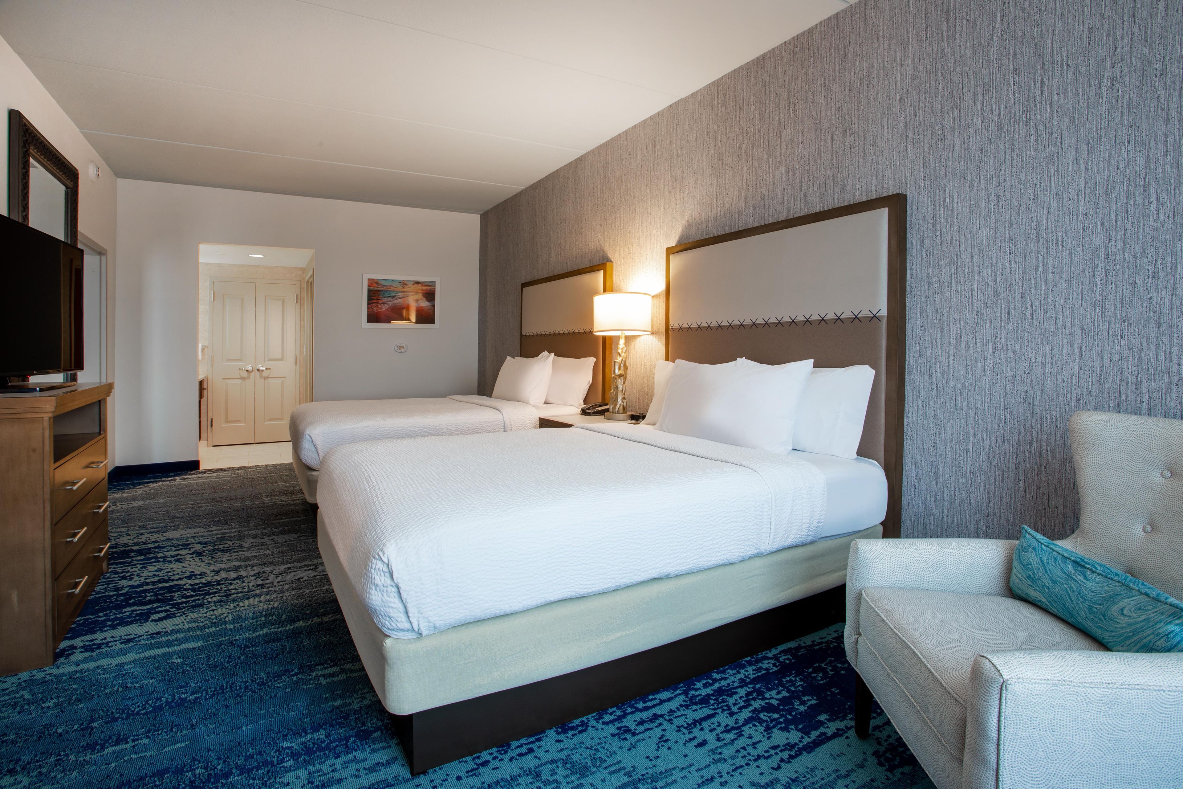 Quarto de hotel com duas camas, televisão, escrivaninha e uma cadeira.