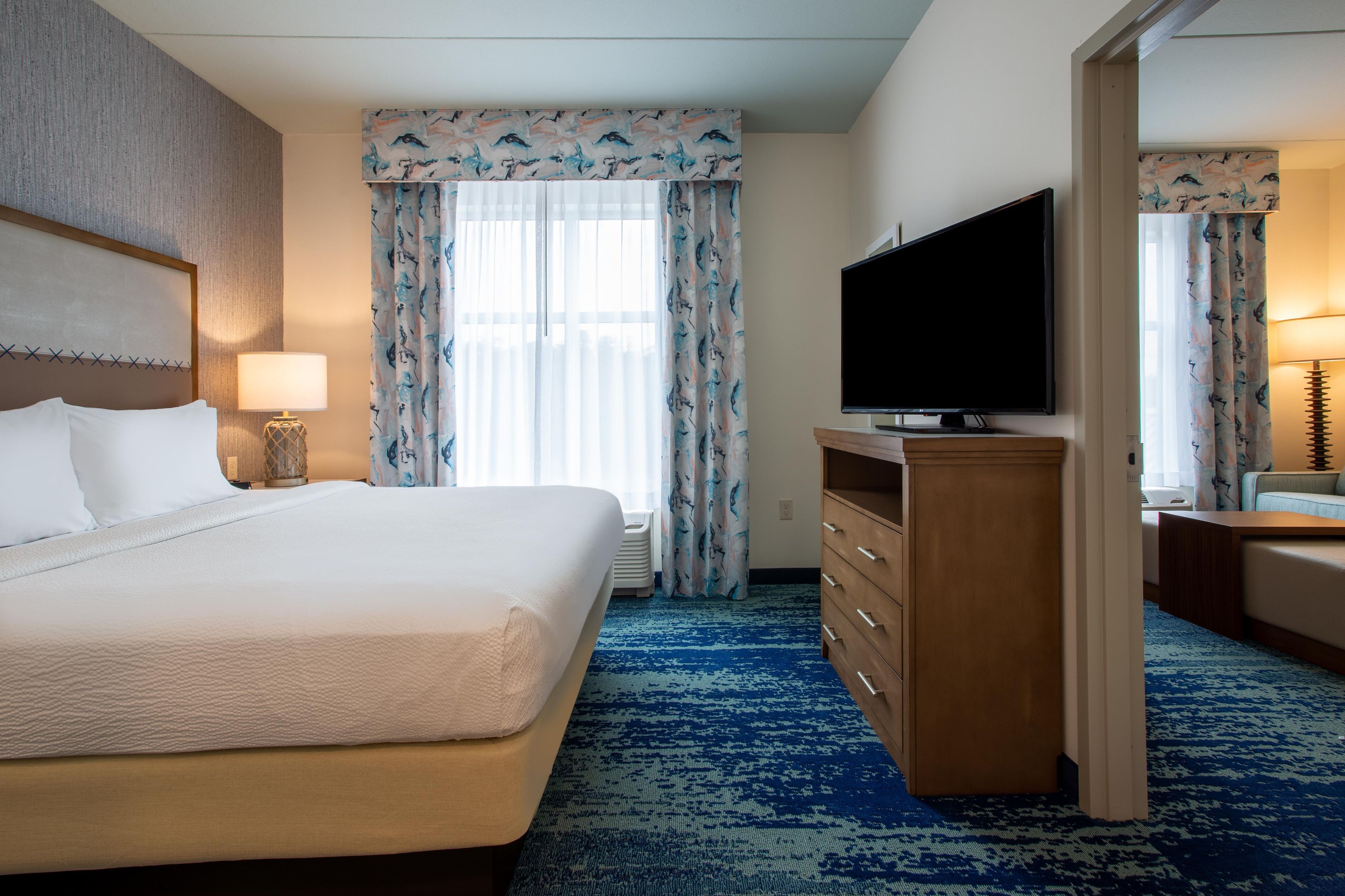 A hotel room with a bed, a television, a dresser, and a window with curtains.