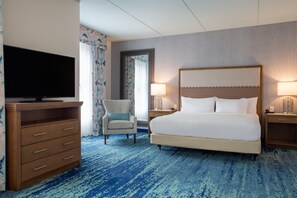 A hotel room with a large bed, a television on a wooden dresser, a chair, and a nightstand with a lamp. - Homewood Suites by Hilton Myrtle Beach Coastal Grand Mall (Myrtle Beach)