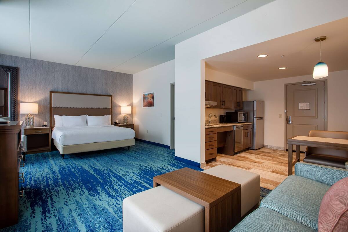 A hotel room with a bed, a desk, a kitchenette, and a bathroom.