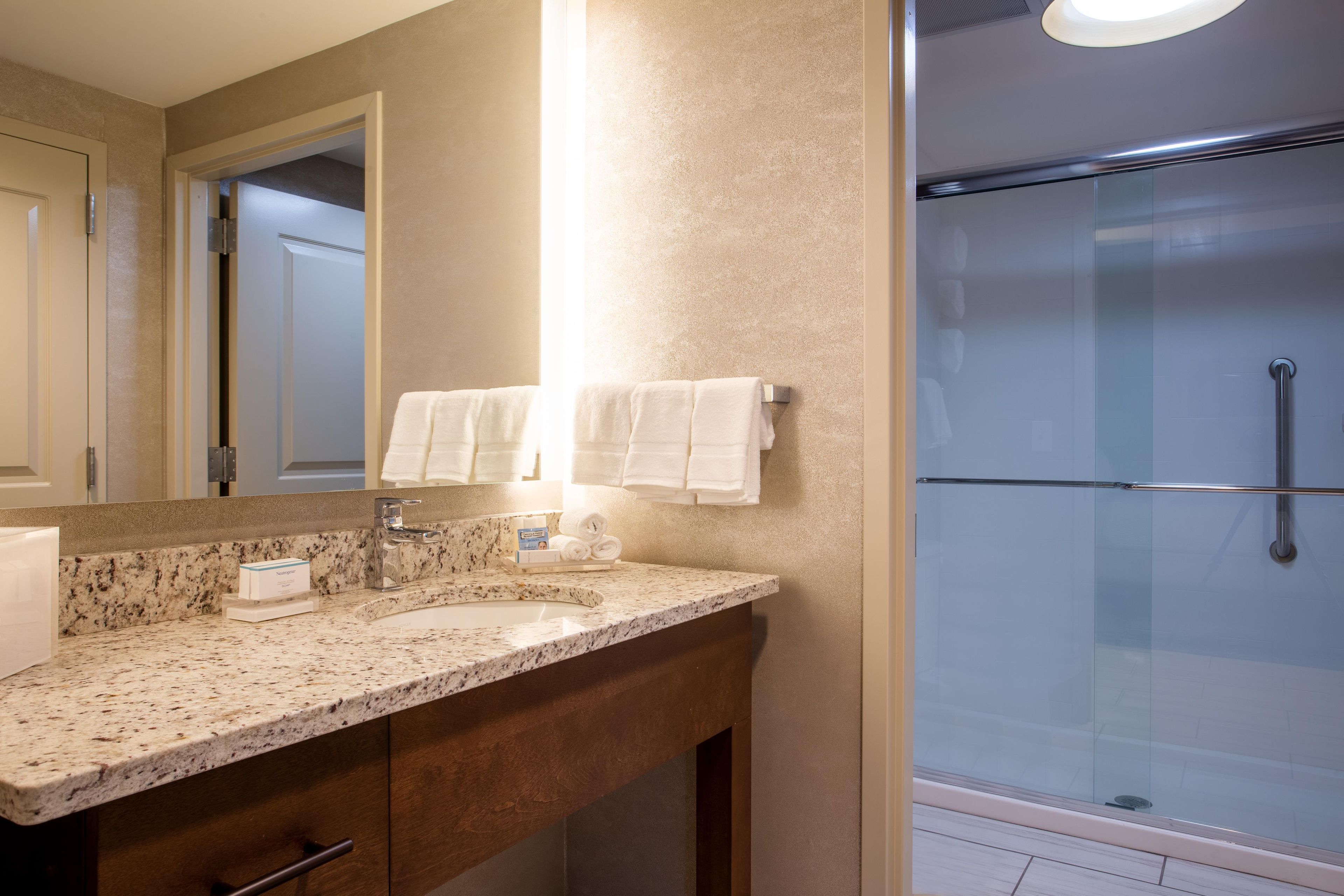 A bathroom with a granite countertop, a mirror, a towel rack, and a glass shower enclosure.
