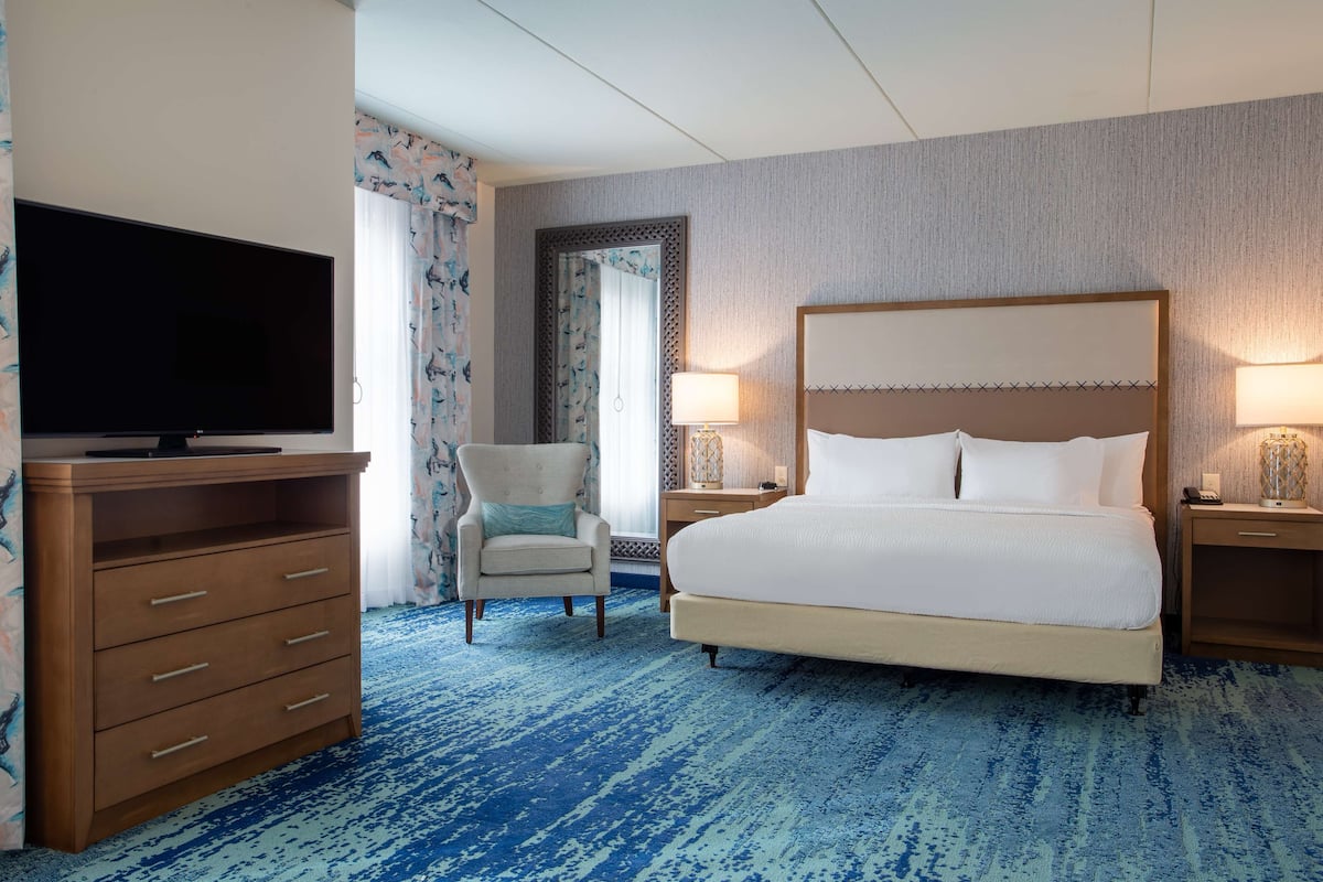 A hotel room with a large bed, a television on a wooden dresser, a chair, and two bedside tables with lamps.