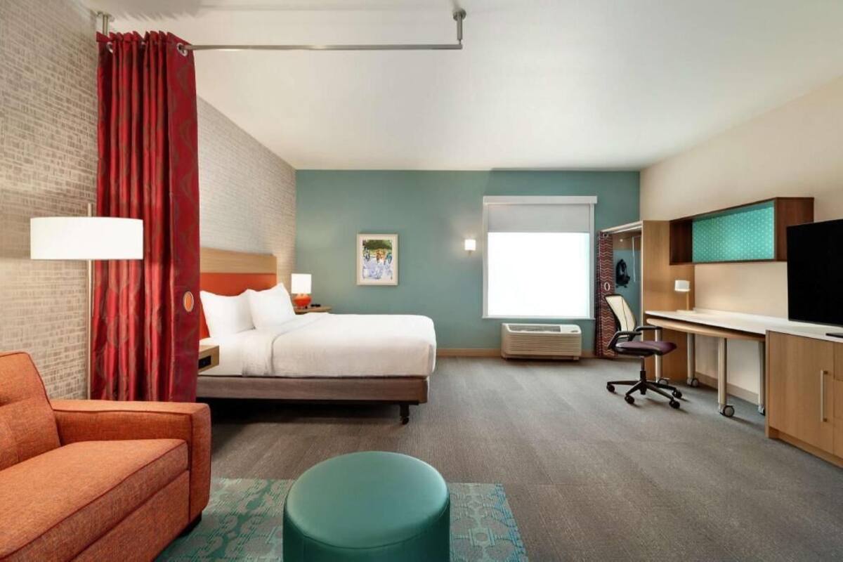 A hotel room with a bed, a desk, a chair, a TV, and a window.