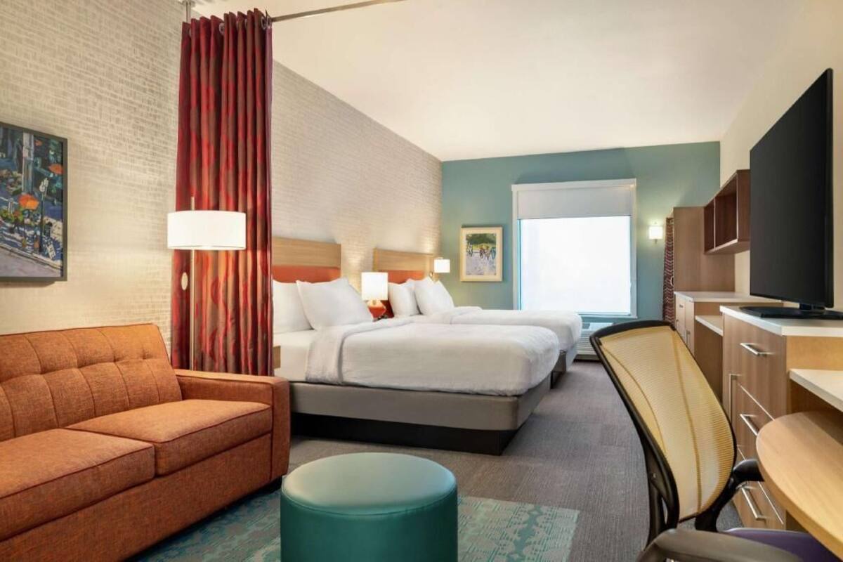 A hotel room with a bed, a sofa, a desk, a television, and a window.