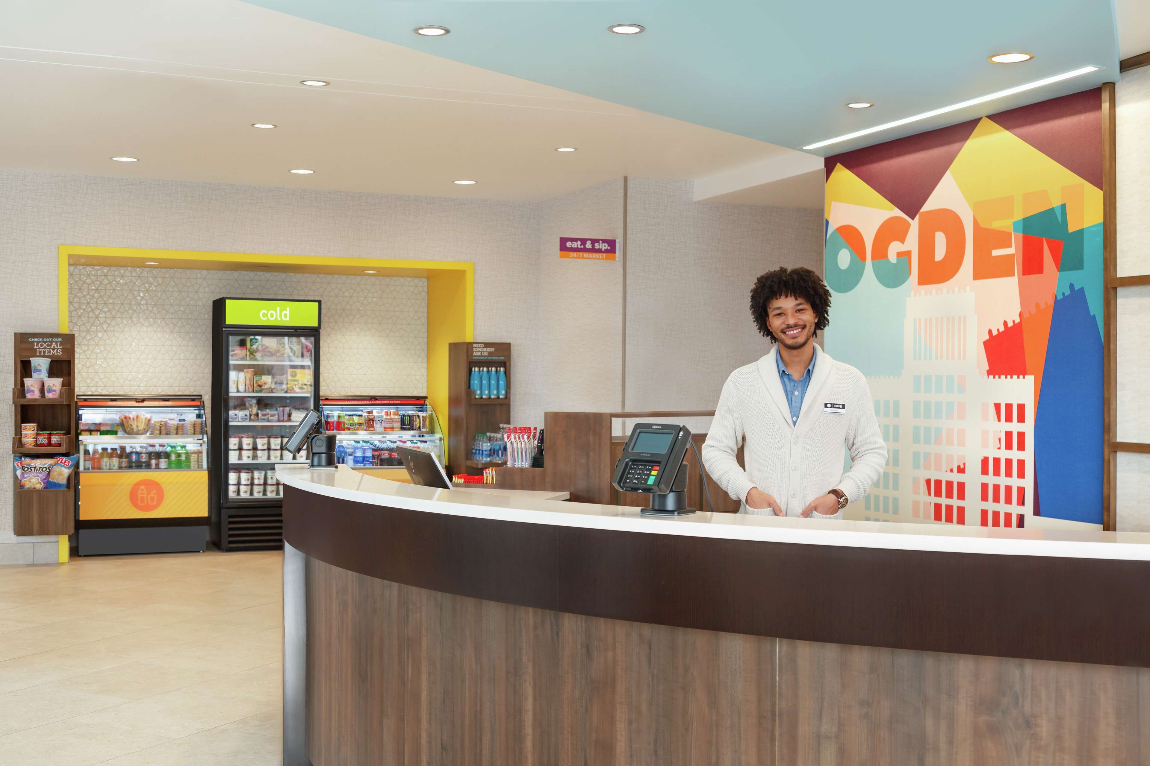 A reception desk with a digital kiosk, a cold food display, and a local items section.