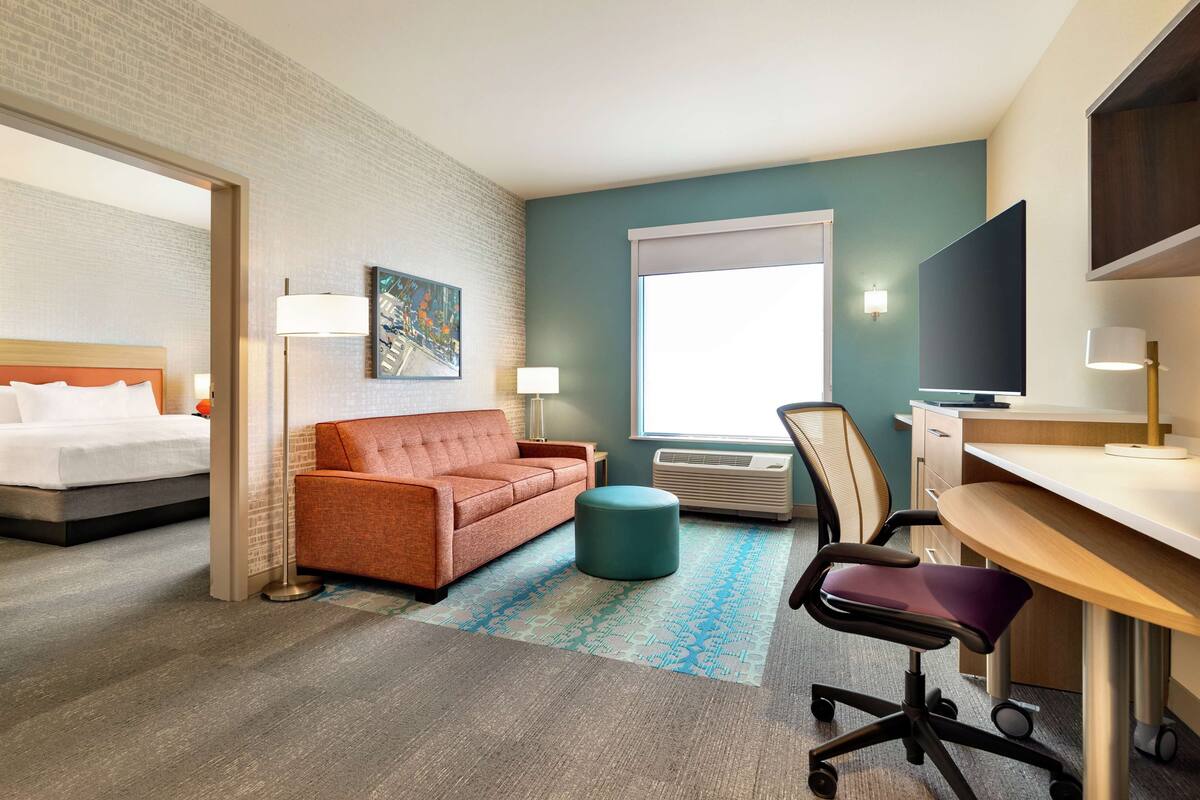 A hotel room with a bed, a sofa, a desk, a chair, a television, and a window.