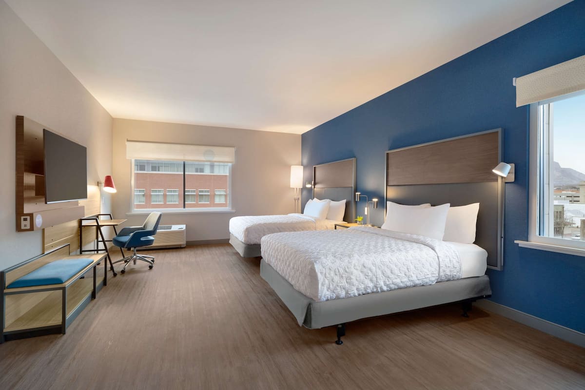 A hotel room with two beds, a desk, a chair, a TV, and a window with a city view.