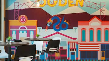 A colorful mural with the word 'OGDEN' and a dragon, tables, chairs, and a plant on a table.