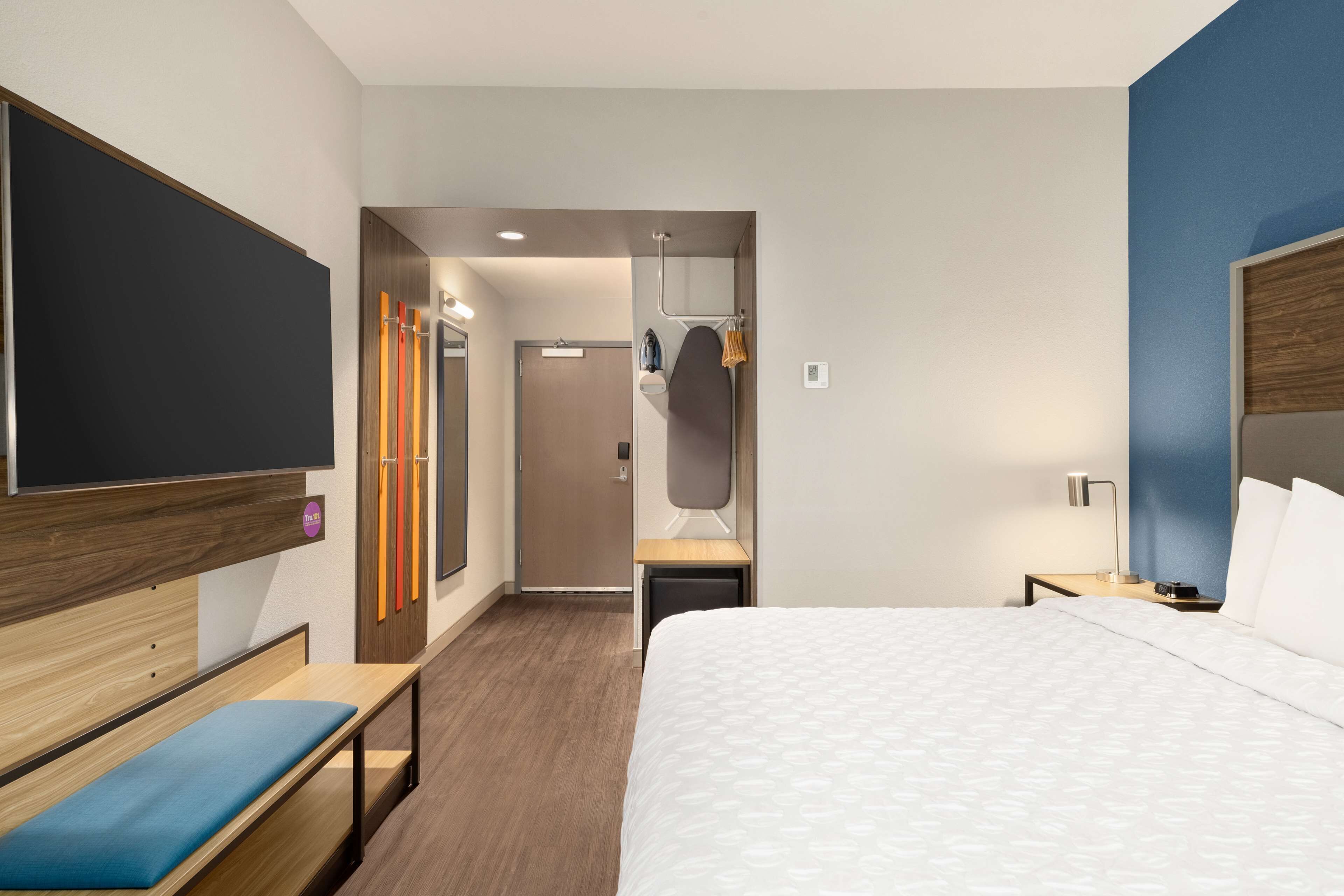 Habitación de hotel con una cama grande, un banco, un armario y un espejo.