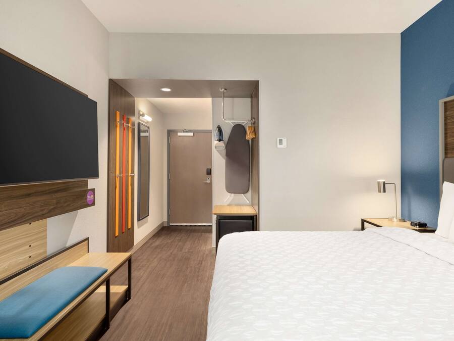 Habitación de hotel con una cama grande, un banco, un armario y un espejo.