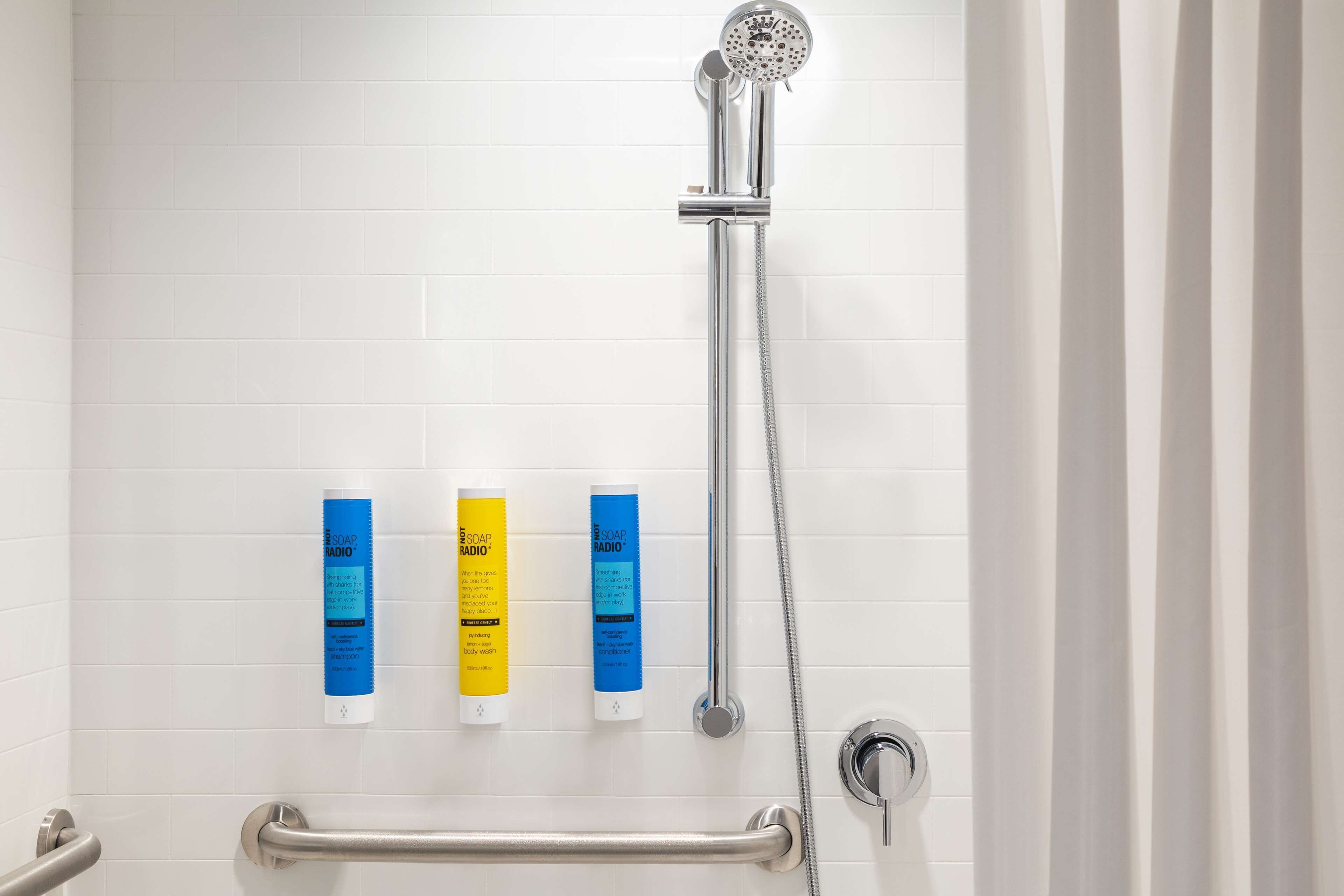 Une douche équipée d’un pommeau de douche à main, d’un distributeur de savon à main et d’un savon en barre.