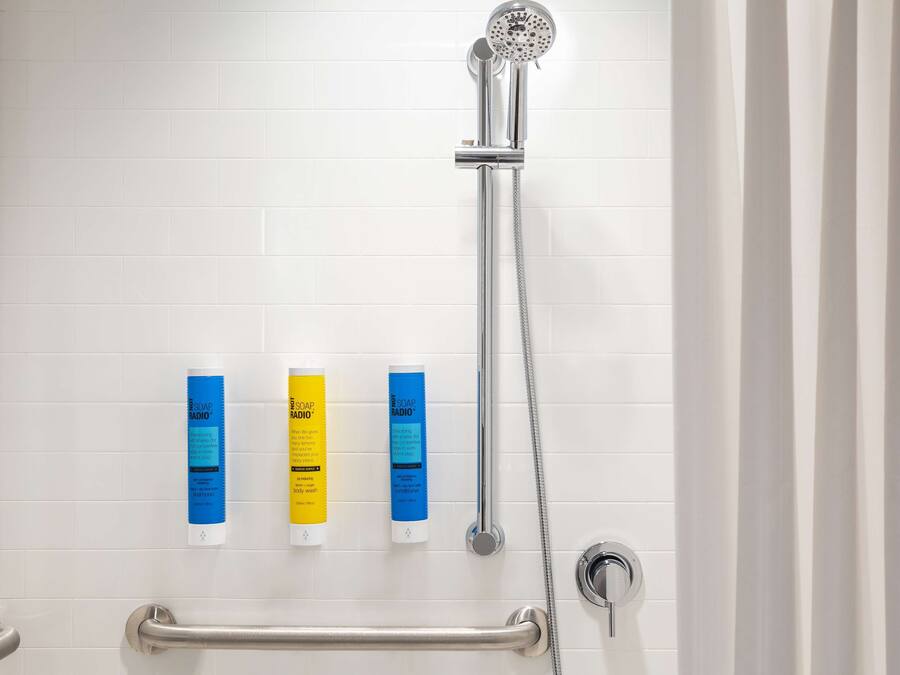 Une douche équipée d’un pommeau de douche à main, d’un distributeur de savon à main et d’un savon en barre.