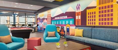A modern lounge area with a pool table, comfortable seating, and a colorful mural depicting a cityscape.