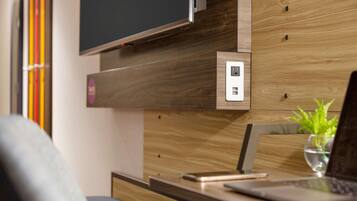 Una habitación moderna con una pared de madera, un televisor de pantalla plana sobre un mueble de madera, una computadora portátil sobre un escritorio y una planta pequeña en un florero de vidrio.
