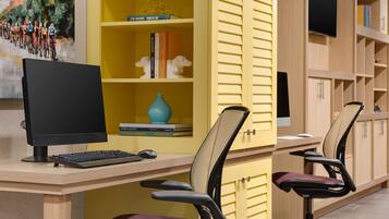 A modern office space with a desk, two chairs, a computer monitor, keyboard, and a bookshelf with books and decorative items.