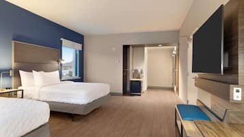 Habitación de hotel con dos camas, un escritorio, una silla, un televisor y vistas a la ciudad.