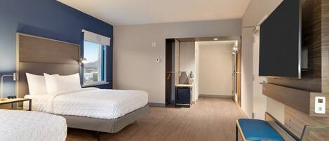 A hotel room with two beds, a desk, a chair, a TV, and a view of the city.