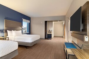 Habitación de hotel con dos camas, un escritorio, una silla, un televisor y vistas a la ciudad.