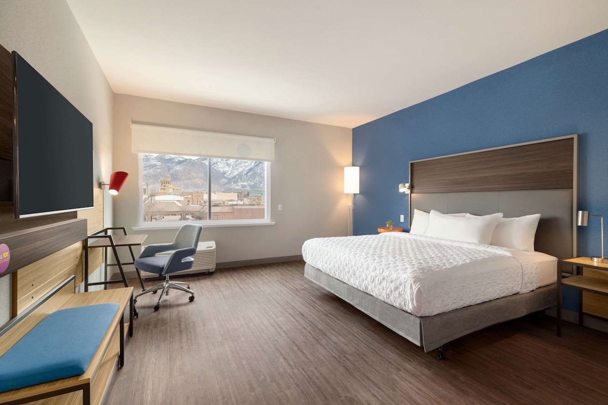 A hotel room with a bed, a desk, a chair, and a window with a mountain view.