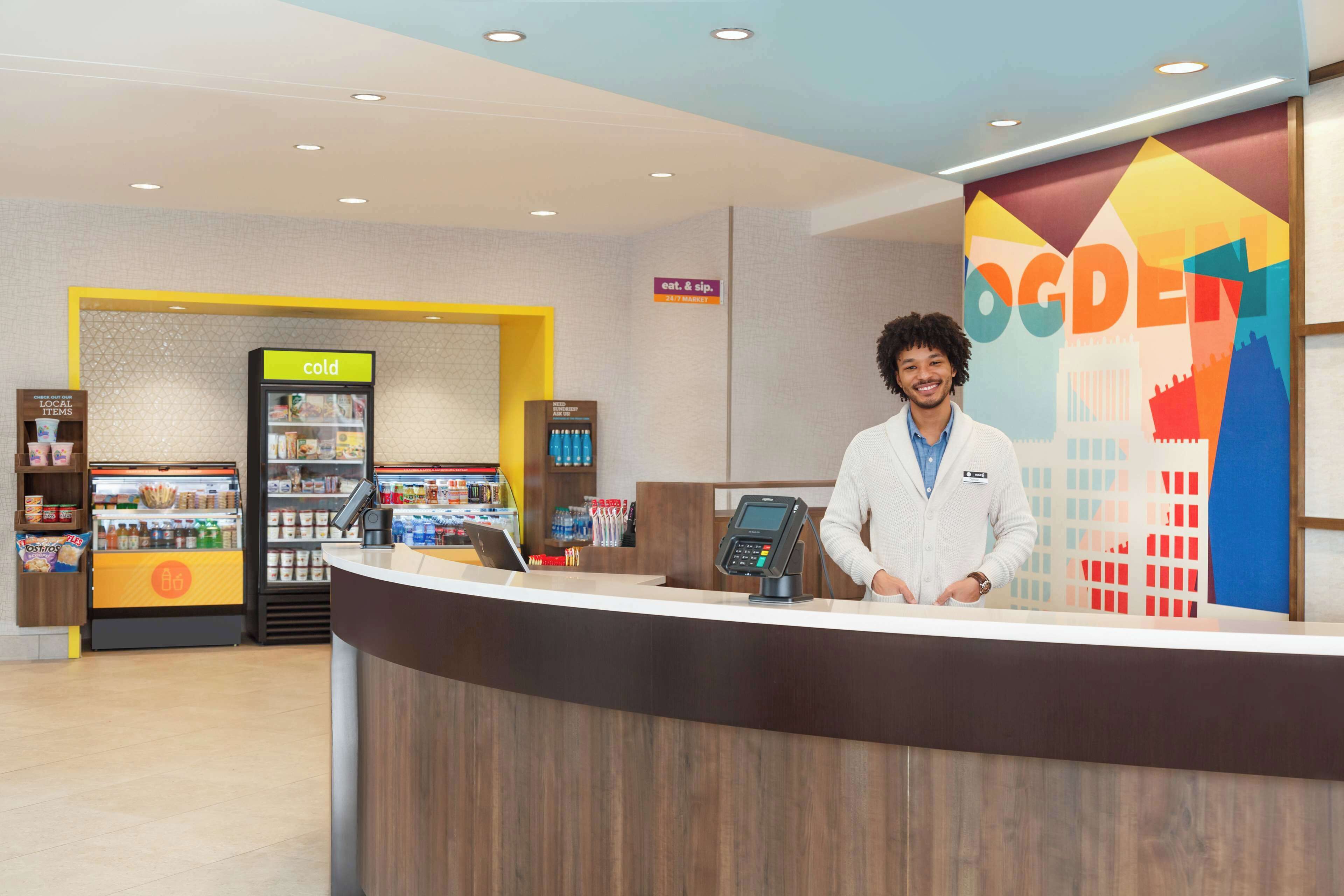 A reception desk with a digital kiosk, a cold beverage fridge, and a local items display.