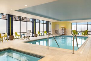 Una piscina interior con agua azul cristalina, sillas amarillas y verdes, y suelo de baldosas.